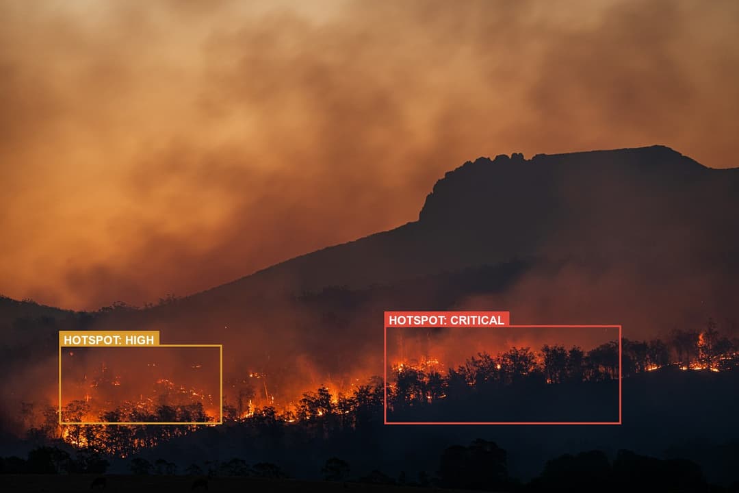 Wildfire burning across a forested hillside at dusk, annotated with critical and high hotspot zones